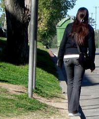 Woman standing on curb, facing downhill, about to step off